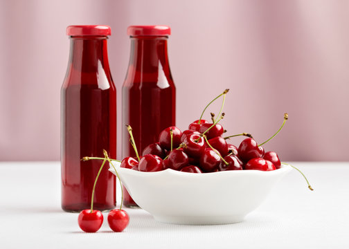 Cherries in a bowl and two bottles of cherry juice.