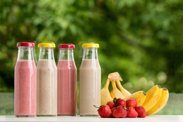 Strawberry and banana smoothie in glass bottle on green backgrou