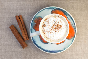 Cappuccino with cinnamon sticks on a table, top view.