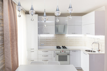 White glossy modern kitchen with stone countertop and built in household appliances in light colors...