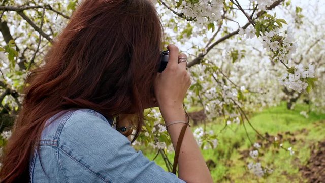 Beautiful young woman taking photos with old film camera of blooming tree. Close up. Slow motion