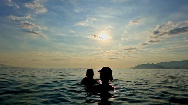 Silhouette of Woman with Toddler in Arms in Sea against Sunset