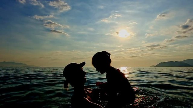Silhouette of Woman with Toddler in Arms in Sea against Sunset