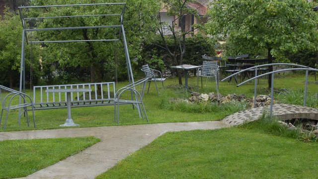 Rain is falling on garden with fountain and mini bridge