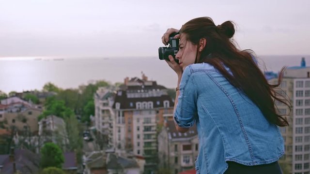 Beautiful young female photographer take photos of cityscape from the roof.  Slow motion