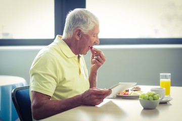 Senior man using digital tablet while having breakfast