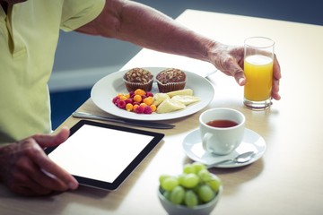 Obraz na płótnie Canvas Senior man using digital tablet while having breakfast