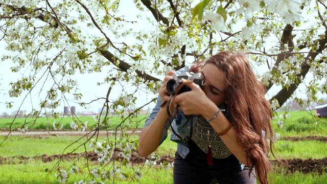 Beautiful young woman taking photos with old film camera of blooming tree. Close up. 