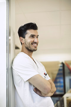 Smiling Young Male Doctor Leaning On Wall In Hospital