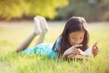 Smiling girl lying on grass and reading book in park