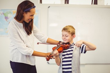 Teacher assisting a schoolboy to play a violin in classroom