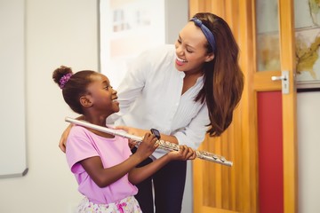 Teacher assisting a girl to play a flute in classroom