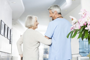Disabled Senior Woman Looking At Mature Physiotherapist