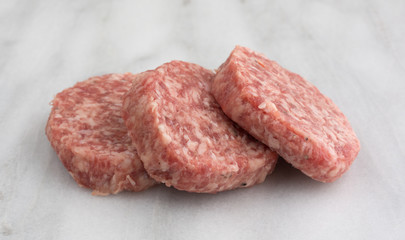 Fresh sausage patties on a marble cutting board side view.