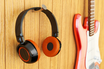 Fototapeta na wymiar Instrumental music listening concept, recording studio equipment, closeup view of modern headphones and electric guitar on wooden wall background