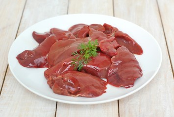 Raw liver on the white plate on the wooden background