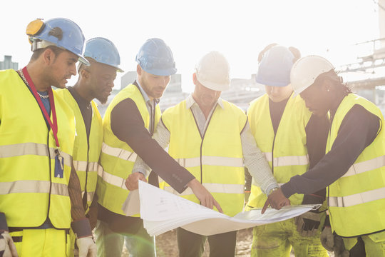 Architect explaining plan on blueprint to construction workers at site