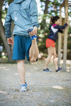Rear view low section of man exercising at outdoor gym with woman in background