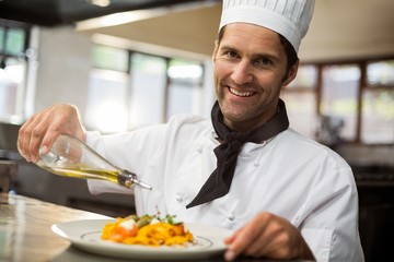 Portrait of happy chef pouring olive oil on meal