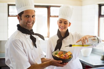 Happy chef pouring olive oil on salad