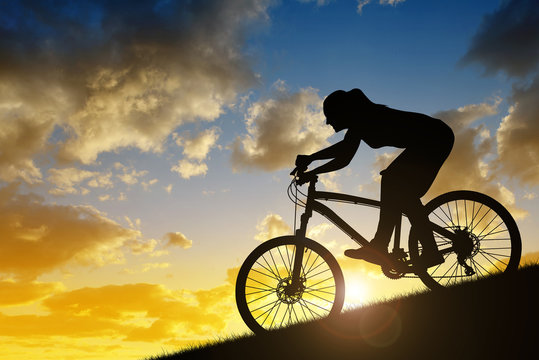 Silhouette of a girl riding a mountain bike down a hill at sunset