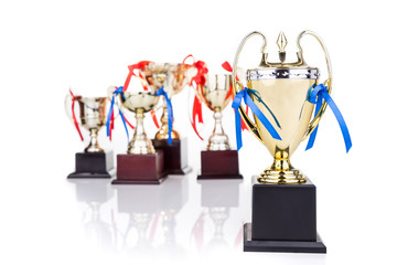 Fototapeta na wymiar Group of gold trophies with decorative ribbons, focusing on one
