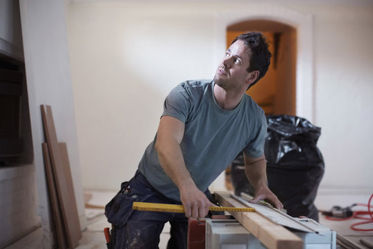 Carpenter looking away while measuring wooden plank at site