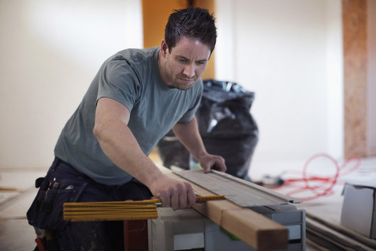 Male carpenter measuring wooden plank at site