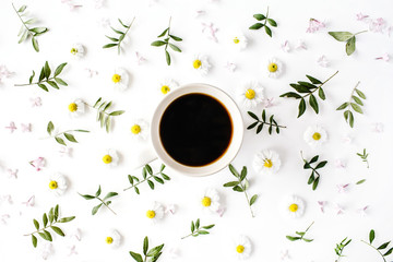 Cup of coffee with chamomile flower and green branches. Flat lay, top view