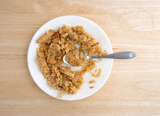 Chicken in a sauce with rice and veggies on a white plate atop a wood table.
