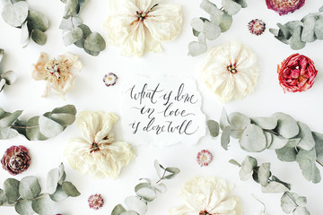quote "what is done in love is done well" written in calligraphy style on paper with pink, red roses, ranunculus, white flowers and leaves isolated on white background. Flat lay