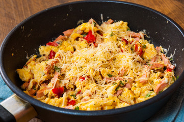 scrambled eggs with ham, vegetables and cheese in a frying pan on wooden table