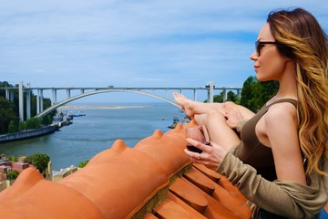 Woman enjoying sunbath with glass of port wine on the rooftop, on river bridge background.