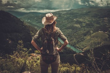 Woman hiker with backpack enjoying amazing valley landscapes on a top of mountain. - 113326295