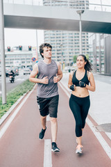 Fototapeta na wymiar Couple of young handsome caucasian man and woman running into the streets of the city, one overlooking left, the other right - sportive, fitness, healthy concept