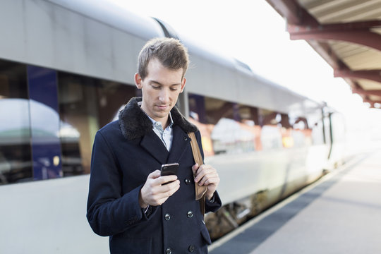 Young businessman using cell phone on railroad station