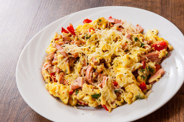 scrambled eggs with ham, vegetables and cheese in a plate on wooden table
