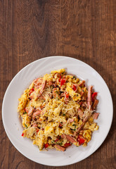scrambled eggs with ham, vegetables and cheese in a plate on wooden table