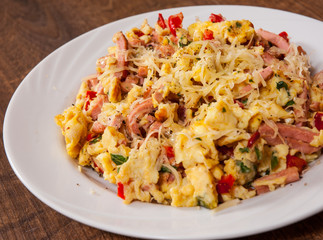 scrambled eggs with ham, vegetables and cheese in a plate on wooden table