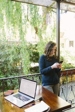 Young woman sitting on balcony using laptop and smart phone