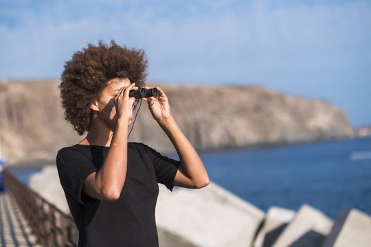 Spain, Tenerife, young woman on a jetty looking at distance with binocular