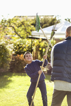 Playful father and son fighting with rakes at garden