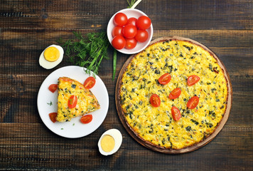 Omelet with herbs and vegetables on wooden background, top view