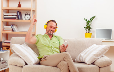 Obraz premium Portrait of handsome man happy listening to music at home. Cheerful man sitting on sofa or couch and showing yo sign to camera.