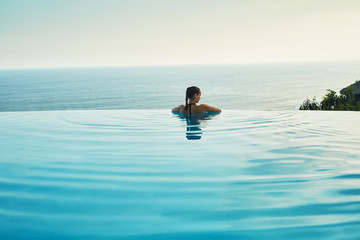 Luxury Resort. Woman Relaxing In Infinity Swimming Pool Water. Beautiful Happy Healthy Female Model...