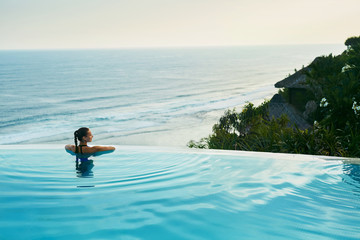 Luxury Resort. Woman Relaxing In Infinity Swimming Pool Water. Beautiful Happy Healthy Female Model...