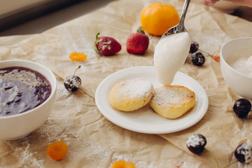 Cheese pancakes with sour cream in spoon. Parchment background