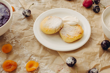Cheese pancakes with sour cream on parchment background