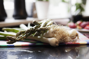 Spring onions and asparagus on cutting board in kitchen