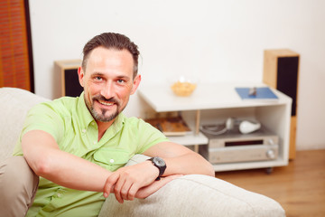 Fototapeta premium Closeup portrait of handsome man resting and relaxing on sofa or couch at home. Happy man smiling and laughing for camera.